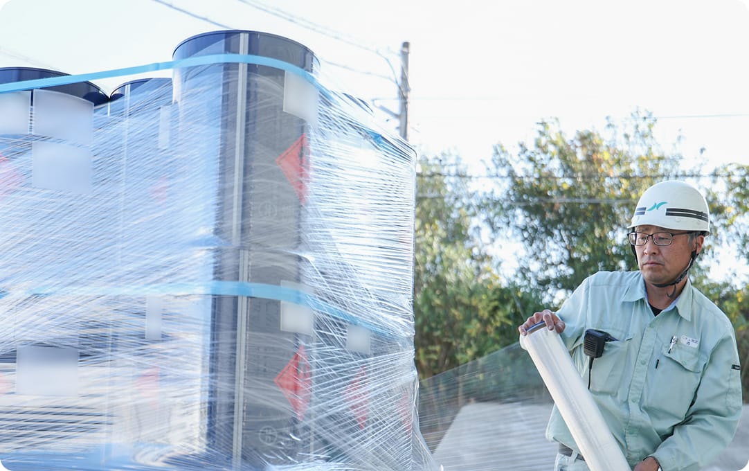 ドラム缶をラップで巻く作業スタッフの写真